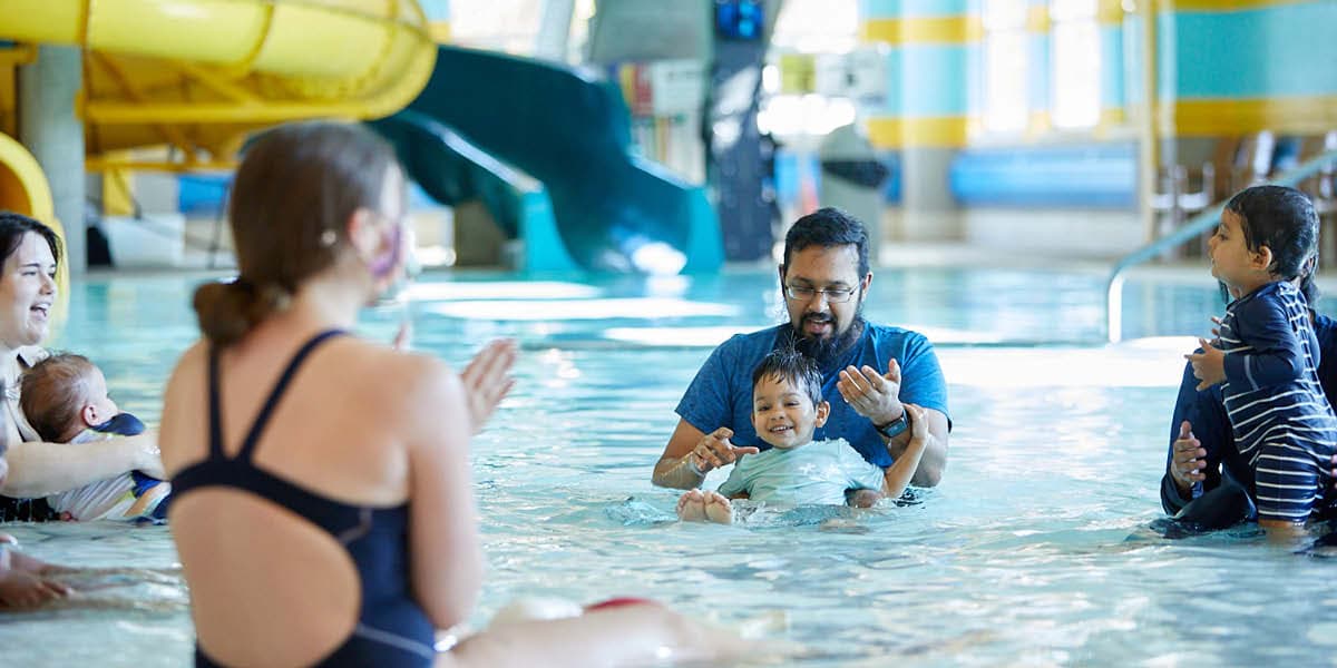 Dad with daughter in his lap getting used to the water in swim lessons