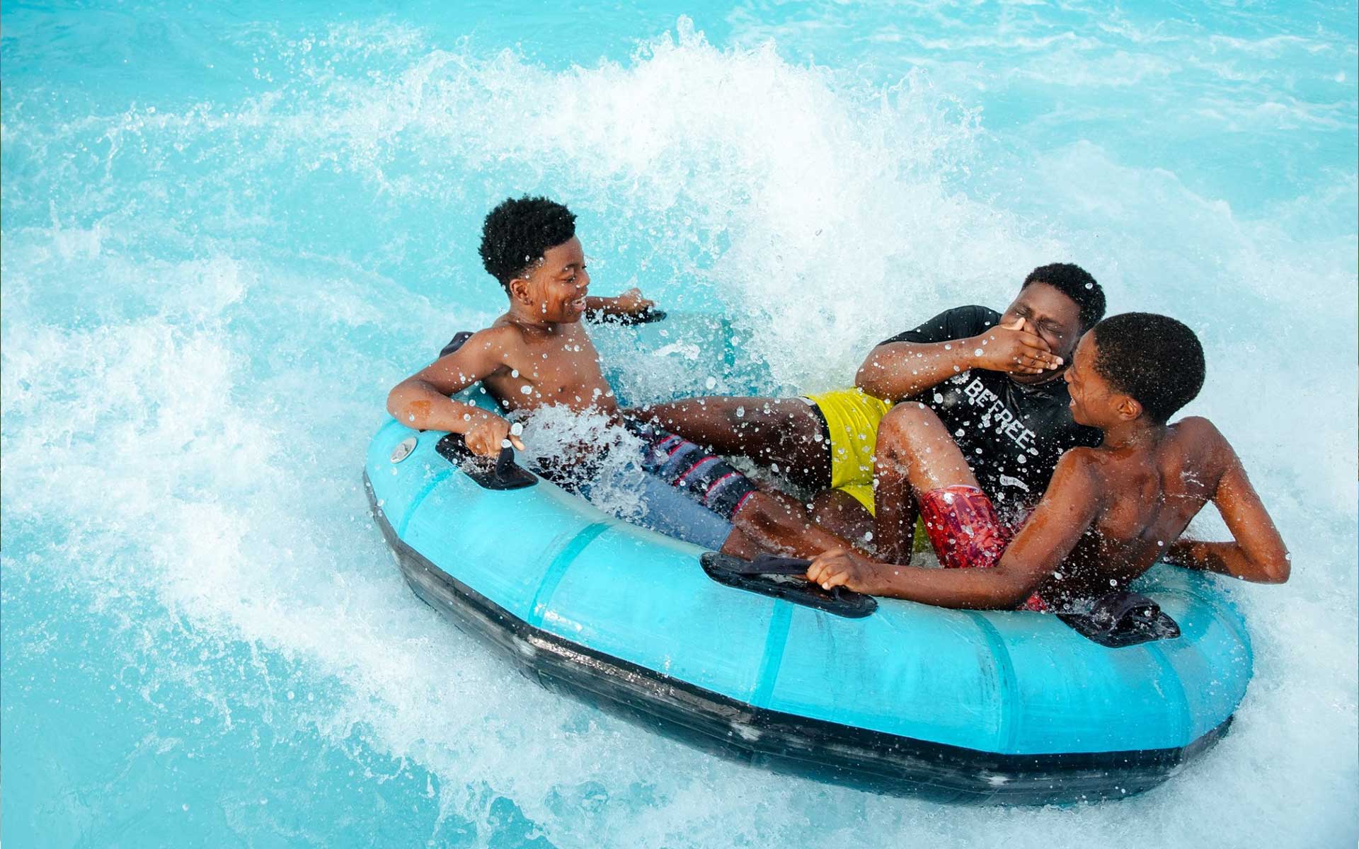 three young black boys on a float splashing in the water