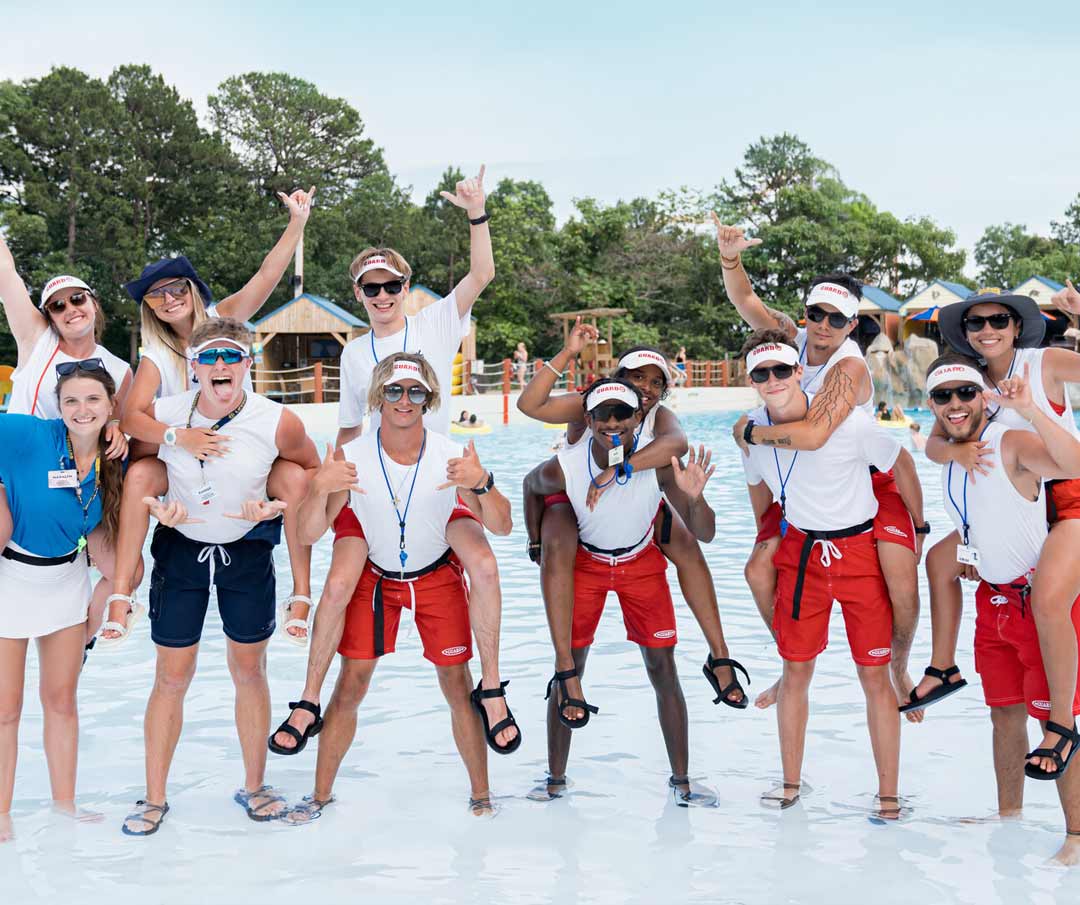 Group of lifeguards laughing and posing for a group photo by the wave pool